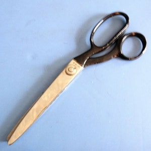 May include: Vintage sewing scissors with a silver blade and dark grey handles. The scissors are approximately 25 cm long, set against a light blue background.