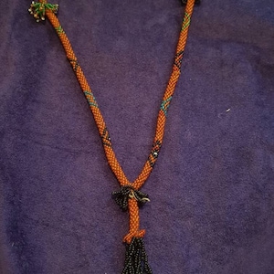 May include: A beaded necklace with a black tassel and a bird charm. The necklace is made of orange, black, and blue beads.