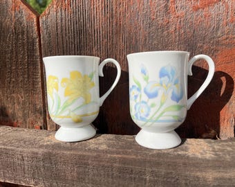 Set van twee porseleinen mokken op voet met bloemenmotief, vintage theekopjes met gele lelie en blauwe iris.