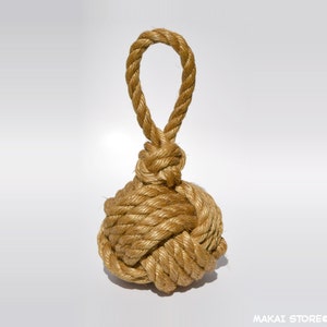 May include: A natural fiber rope doorstop with a knotted ball shape and a loop at the top. The doorstop is a light brown color.