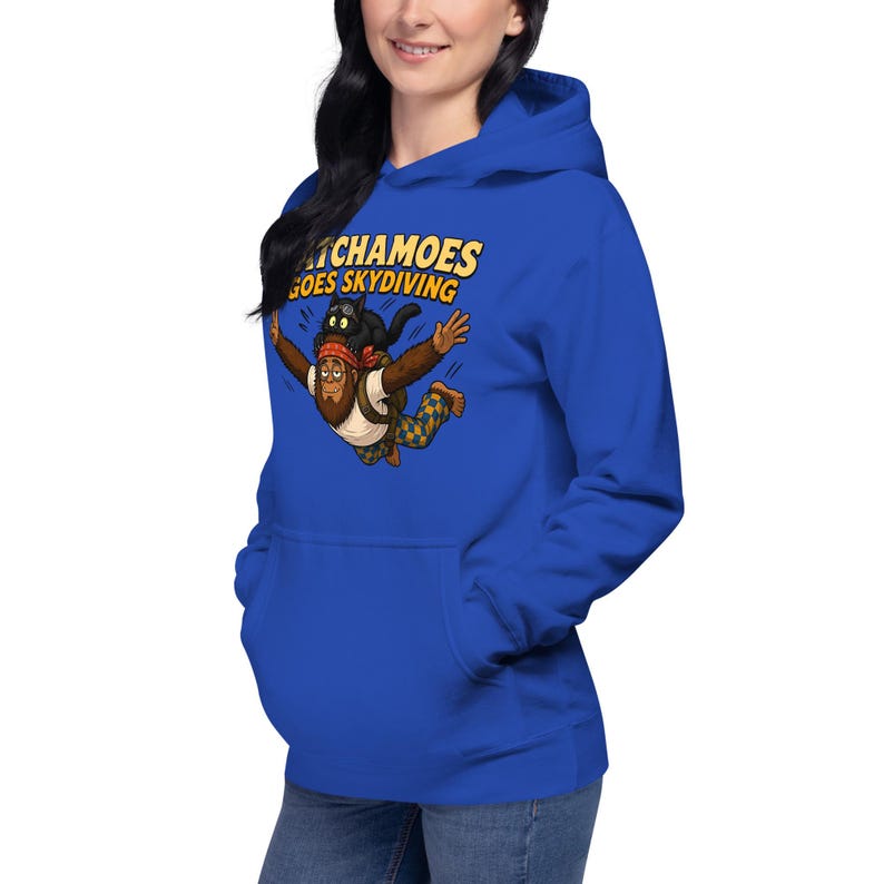 May include: A royal blue hoodie featuring a graphic of a brown creature with a red bandana and blue and yellow checkered pants skydiving with a black cat on its head. The text above the graphic reads "PATCHAMOES GOES SKYDIVING" in yellow.