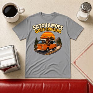 Könnte beinhalten: Ein graues T-Shirt mit einer Grafik eines orangefarbenen Vans, der auf einer Straße vor einem Sonnenuntergang fährt. Der Text SATCHAMOES GOES CRUISING ist in Gelb über dem Van gedruckt. Eine Figur ist am Steuer zu sehen.