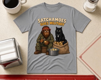 May include: A gray t-shirt featuring a cartoon graphic of a brown creature in camouflage clothing peeling a potato next to a black cat sitting on a burlap sack of potatoes. The text above reads SATCHAMOES GOES MILITARY in yellow letters.