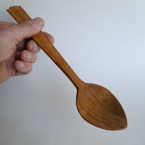 May include: A wooden spoon with a long, narrow handle and a rounded, oval-shaped bowl. The spoon is made of light brown wood and has a natural, rustic finish.