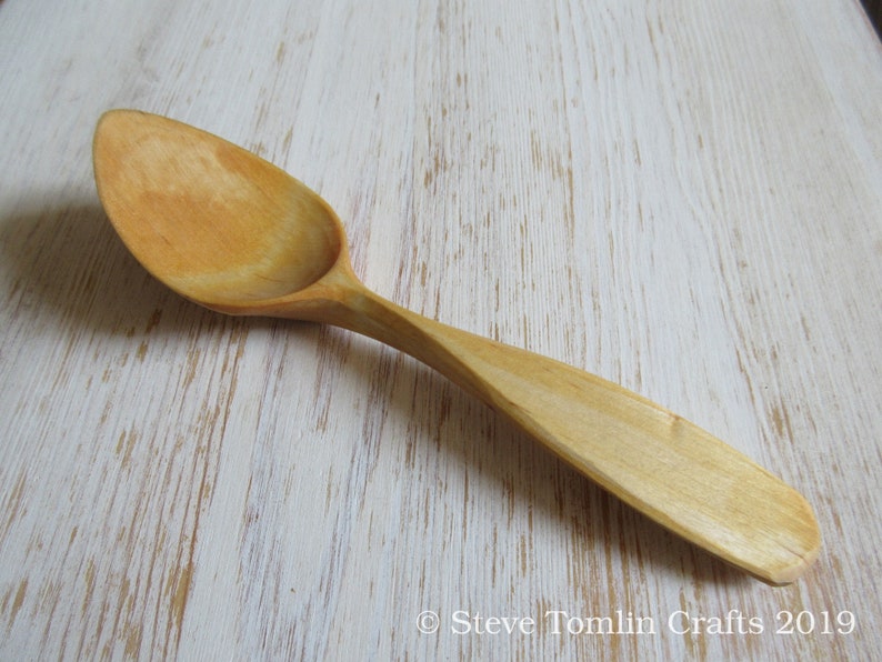 May include: A wooden spoon with a light brown color and a smooth, rounded surface. The spoon is made of natural wood and has a long handle.