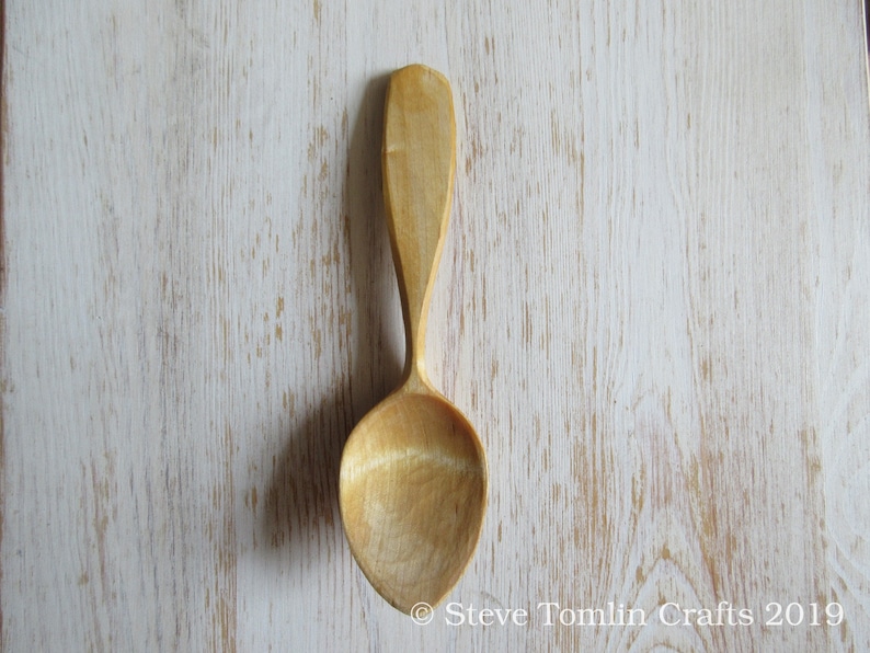 May include: A wooden spoon with a natural finish. The spoon has a long handle and a rounded bowl.