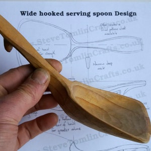 May include: A wooden serving spoon with a wide, hooked handle. The spoon is made of light brown wood and has a deep bowl. The spoon is being held in a hand, and the background is a white sheet of paper with a drawing of a spoon on it.