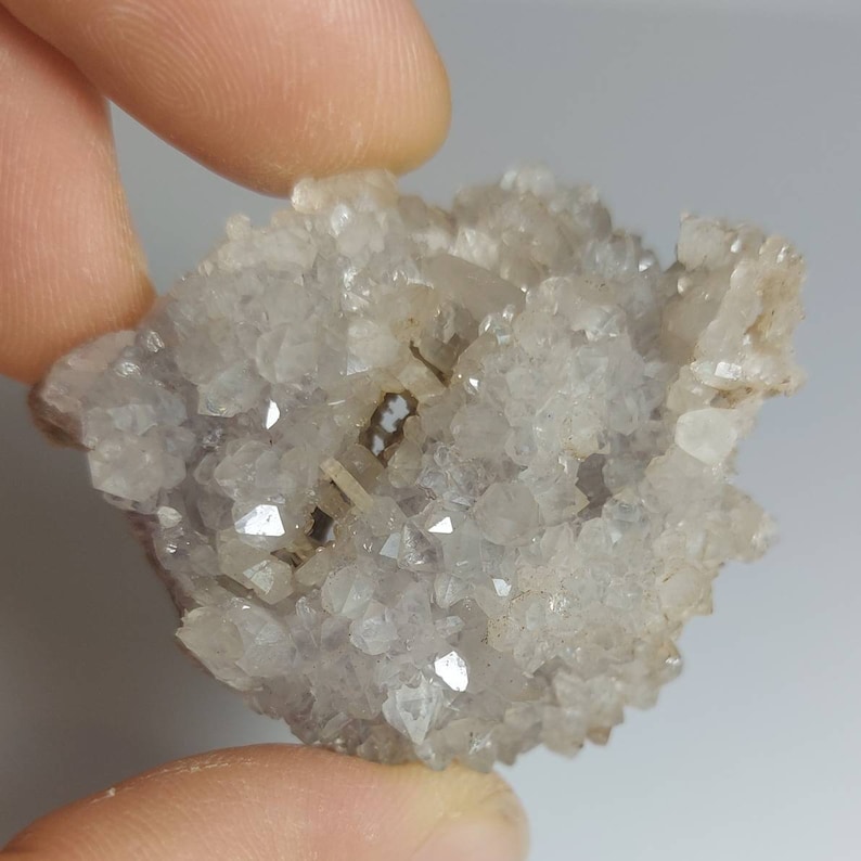 May include: A cluster of small, clear quartz crystals with a hint of purple. The crystals are clustered together in a rough, natural formation.