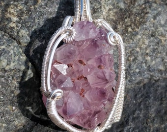 May include: A silver wire-wrapped pendant featuring a cluster of amethyst crystals. The crystals are a deep purple color and have a natural, rough texture. The pendant is a unique and beautiful piece of jewelry.