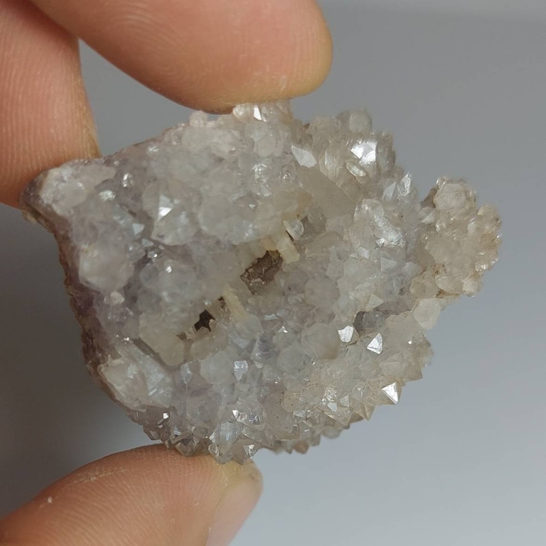 May include: A cluster of small, clear quartz crystals with a hint of purple. The crystals are clustered together in a rough, natural formation.