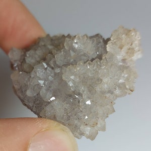 May include: A cluster of small, clear quartz crystals with a hint of purple. The crystals are clustered together in a rough, natural formation.