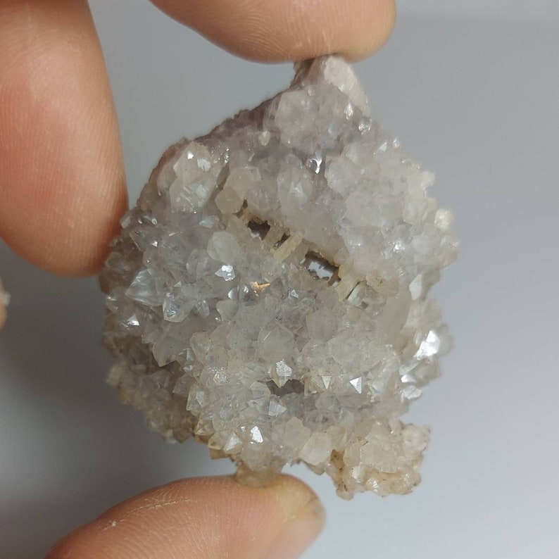 May include: A cluster of small, clear quartz crystals with a hint of purple amethyst. The crystals are clustered together in a rough, natural formation.