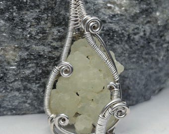May include: A handcrafted pendant featuring a pale yellow crystal encased in a silver wire wrap. The wire is intricately coiled and shaped, creating a decorative frame around the stone. The pendant is designed to be worn as jewelry.