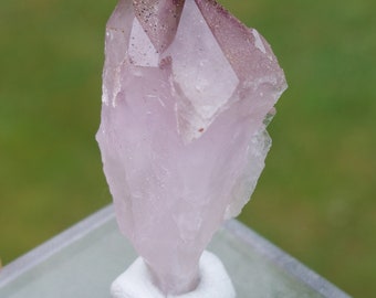 May include: A pale pink amethyst crystal with a double termination. The crystal has a slight purple hue and is displayed on a white base.