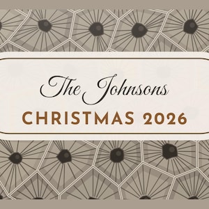 May include: A rectangular sign with rounded corners featuring a cream-colored center panel with the text The Johnsons CHRISTMAS 2026 in black and brown. The background displays a repeating pattern of gray geometric shapes with dark centers.