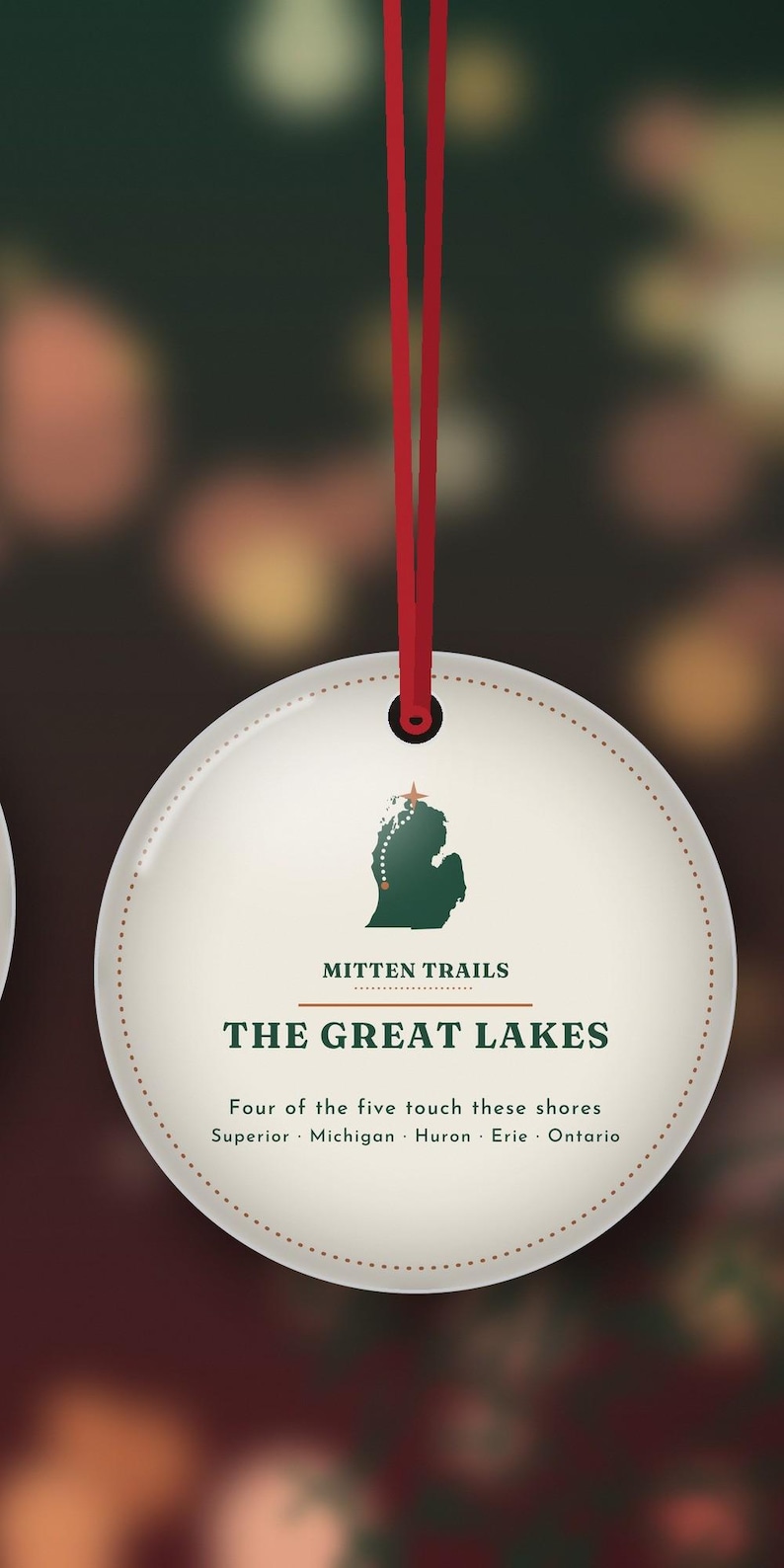 May include: A round white ornament hanging from a red ribbon. It features a green silhouette of Michigan with a star, the text MITTEN TRAILS, THE GREAT LAKES, and the words Four of the five touch these shores Superior Michigan Huron Erie Ontario.