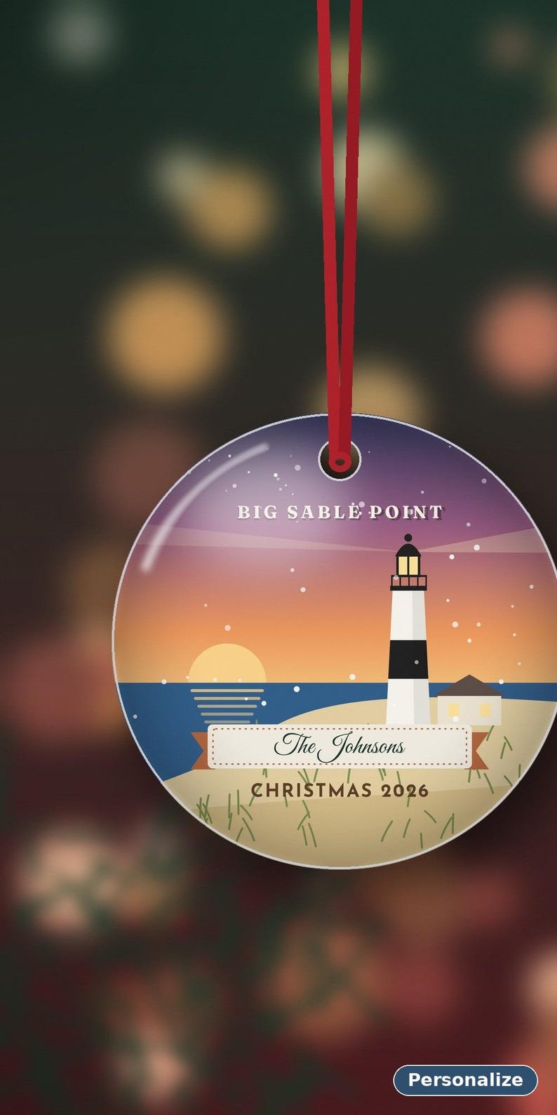 May include: A round, flat ornament hanging from a red ribbon, featuring a graphic of the Big Sable Point lighthouse at sunset. The design includes the text BIG SABLE POINT, The Johnsons, and CHRISTMAS 2026. The scene depicts a beach, ocean, and sky.
