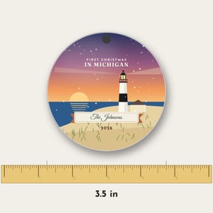 Puede incluir: Un adorno redondo de 8,89 cm de di&aacute;metro, con una ilustraci&oacute;n de un faro al atardecer y el texto "FIRST CHRISTMAS IN MICHIGAN", "The Johnsons" y "2026" impreso sobre un paisaje de playa arenosa bajo un cielo estrellado.