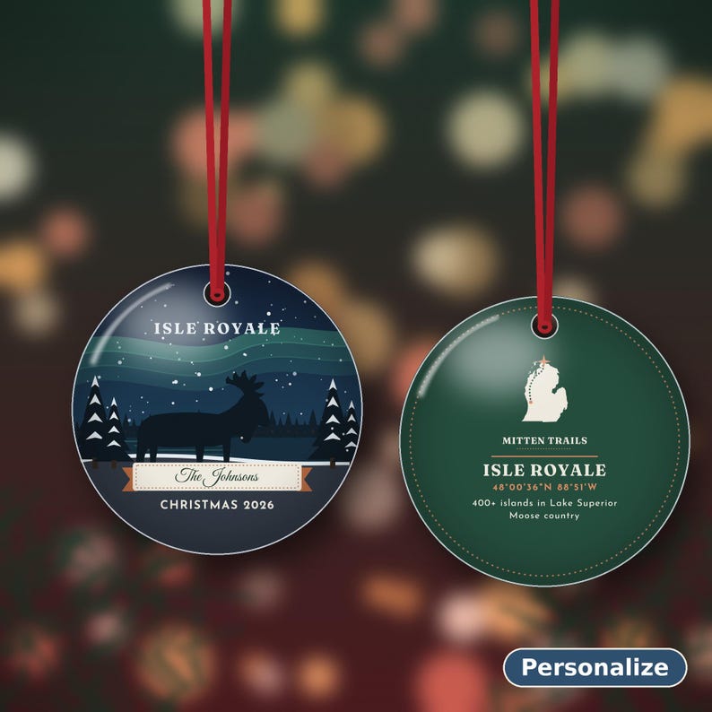 May include: Two round, flat Christmas ornaments with red hanging ribbons. The left ornament features a dark blue night scene with a moose, pine trees, and the text "ISLE ROYALE", "The Johnsons", and "CHRISTMAS 2026". The right ornament is green with a white map outline, "MITTEN TRAILS", "ISLE ROYALE", coordinates, and text about Lake Superior.