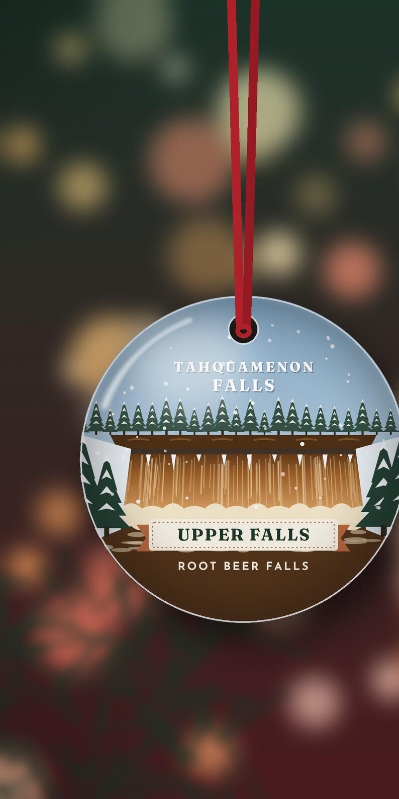 Puede incluir: Un adorno redondo de cer&aacute;mica colgado de una cinta roja, con una ilustraci&oacute;n gr&aacute;fica de Tahquamenon Falls. El dise&ntilde;o incluye una cascada marr&oacute;n, pinos verdes y el texto Tahquamenon Falls, Upper Falls y Root Beer Falls.