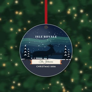 May include: A round Christmas ornament featuring a dark blue night sky with a green aurora, a silhouette of a moose, and pine trees. Text reads ISLE ROYALE, The Johnsons, and CHRISTMAS 2026. It hangs from a thin red ribbon.