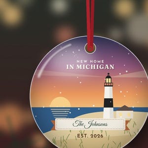 K&ouml;nnte beinhalten: Ein runder, flacher H&auml;ngeschmuck mit einer Leuchtturm-Illustration bei Sonnenuntergang. Der Text lautet NEW HOME IN MICHIGAN, The Johnsons und EST. 2026. Das Design zeigt einen Strand, ein dunkelblaues Meer und einen violetten Sternenhimmel. Ein rotes Band ist befestigt.