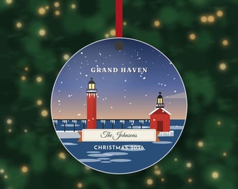 May include: A round Christmas ornament featuring a red lighthouse and pier in Grand Haven during a snowy night. The design includes the text Grand Haven, The Johnsons, and Christmas 2026. A red ribbon is attached to the top for hanging.