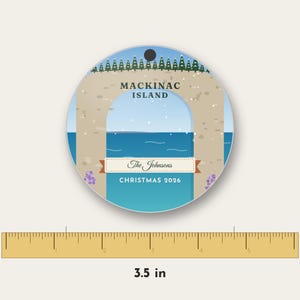 May include: A round ceramic ornament featuring a graphic of Arch Rock on Mackinac Island with a blue sky, water, and pine trees. The text reads MACKINAC ISLAND, The Johnsons, and CHRISTMAS 2026. A ruler shows a diameter of 3.5 inches.