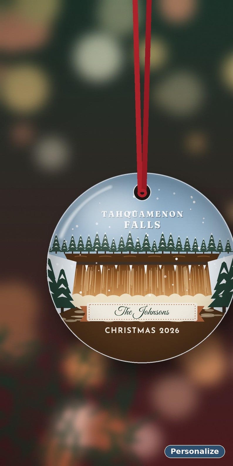 May include: A round, flat, white ceramic ornament hanging from a red ribbon. It features a graphic of Tahquamenon Falls with green pine trees, brown water, and white snow. Text reads: TAHQUAMENON FALLS, The Johnsons, and CHRISTMAS 2026.