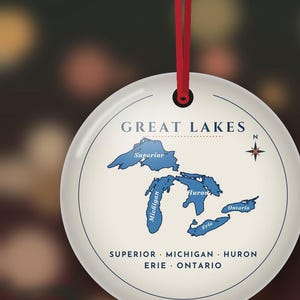 May include: A round white ceramic ornament hanging from a red ribbon. The center features a blue map of the Great Lakes labeled Superior, Michigan, Huron, Erie, and Ontario. The text GREAT LAKES is printed above, with the names listed below.