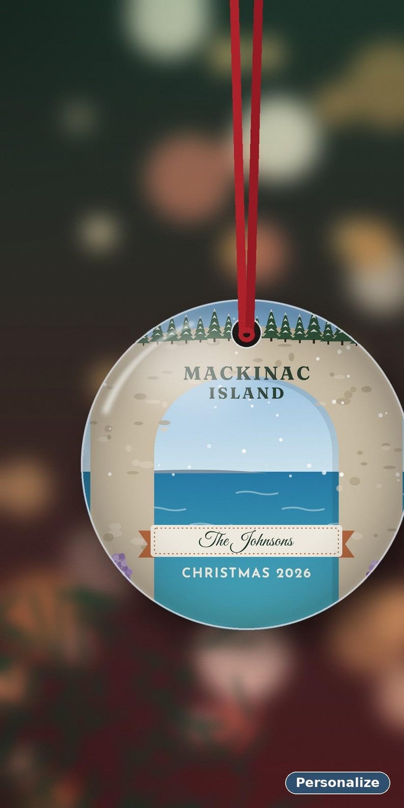 May include: A round, flat Christmas ornament hanging from a red ribbon. The design features a stylized illustration of Mackinac Island with green pine trees, a blue sky, and water. It includes the text "MACKINAC ISLAND", "The Johnsons", and "CHRISTMAS 2026".