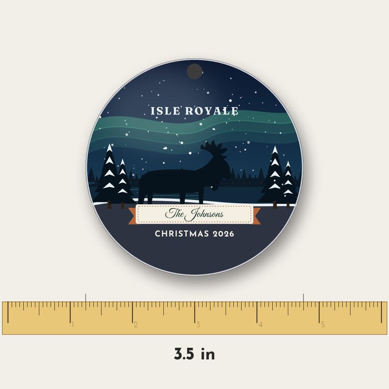 May include: A round Christmas ornament featuring a dark blue night sky with a green aurora, a silhouette of a moose, and pine trees. It displays the text ISLE ROYALE, The Johnsons, and CHRISTMAS 2026. A ruler shows a diameter of 3.5 inches.