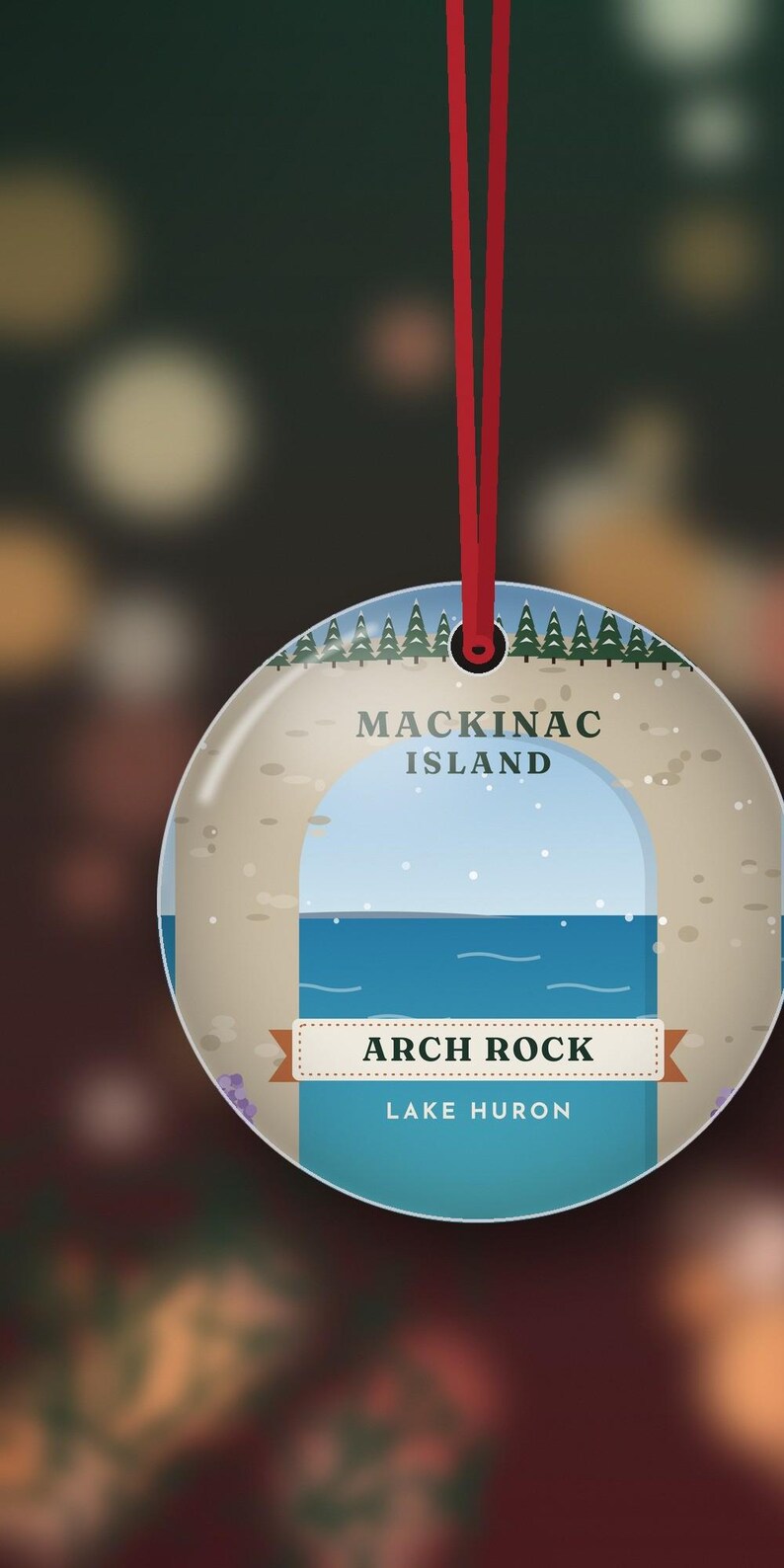 May include: A round, flat ornament hanging from a red ribbon. The design features a graphic illustration of Arch Rock on Mackinac Island, Lake Huron, with a blue sky, water, and a line of green pine trees at the top. The text reads Mackinac Island, Arch Rock, and Lake Huron.