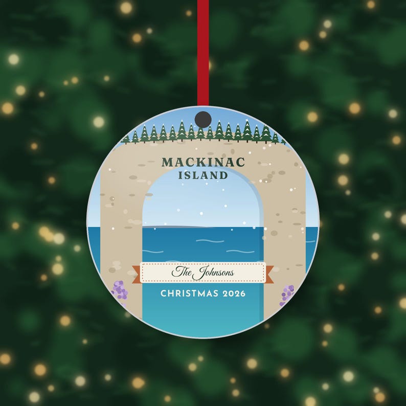 May include: A round ceramic Christmas ornament featuring a graphic illustration of the Arch Rock on Mackinac Island. The design includes a blue sky, a line of green pine trees, blue water, and the text Mackinac Island, The Johnsons, and Christmas 2026.