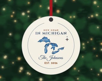 May include: A round, cream-colored ornament hanging from a red ribbon. It features a blue map of the Great Lakes, a compass rose, and the text: NEW HOME IN MICHIGAN, The Johnsons, and EST. 2026. The design is enclosed within a thin circular line.