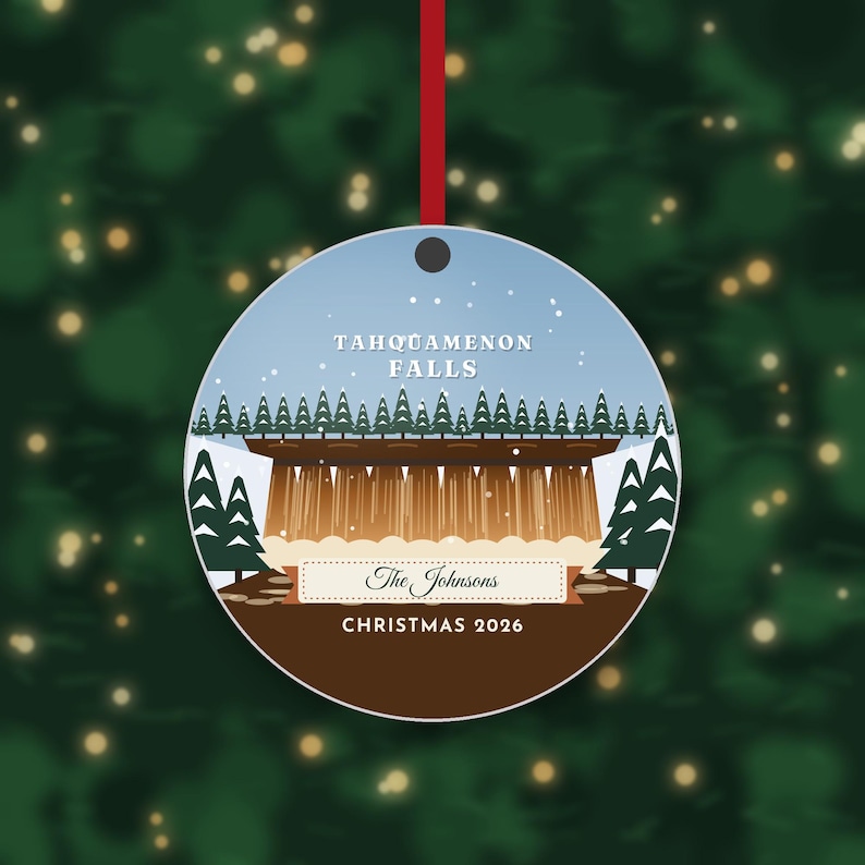 May include: A round Christmas ornament featuring a graphic illustration of Tahquamenon Falls with evergreen trees, a light blue sky, and white snow. The text reads Tahquamenon Falls, The Johnsons, and Christmas 2026, hanging by a red ribbon.