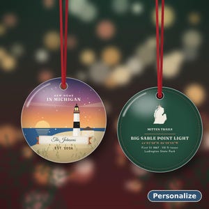 K&ouml;nnte beinhalten: Zwei runde Keramikornamente mit roten Aufh&auml;ngeschleifen. Das linke Ornament zeigt eine Leuchtturmszene in Michigan mit dem Text 'NEW HOME IN MICHIGAN', 'The Johnsons' und 'EST. 2026'. Das rechte Ornament ist dunkelgr&uuml;n mit einer wei&szlig;en Michigan-Karte, 'MITTEN TRAILS', 'BIG SABLE POINT LIGHT', Koordinaten und historischen Fakten.