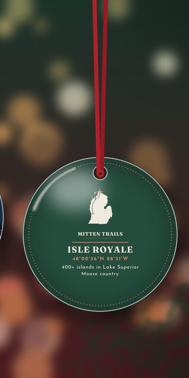 May include: A round, dark green ornament hanging from a red ribbon. It features a white map of Isle Royale, the text "MITTEN TRAILS", "ISLE ROYALE", "48&deg;00'36"N 88&deg;51'W", and "400+ islands in Lake Superior" with "Moose country" printed below.