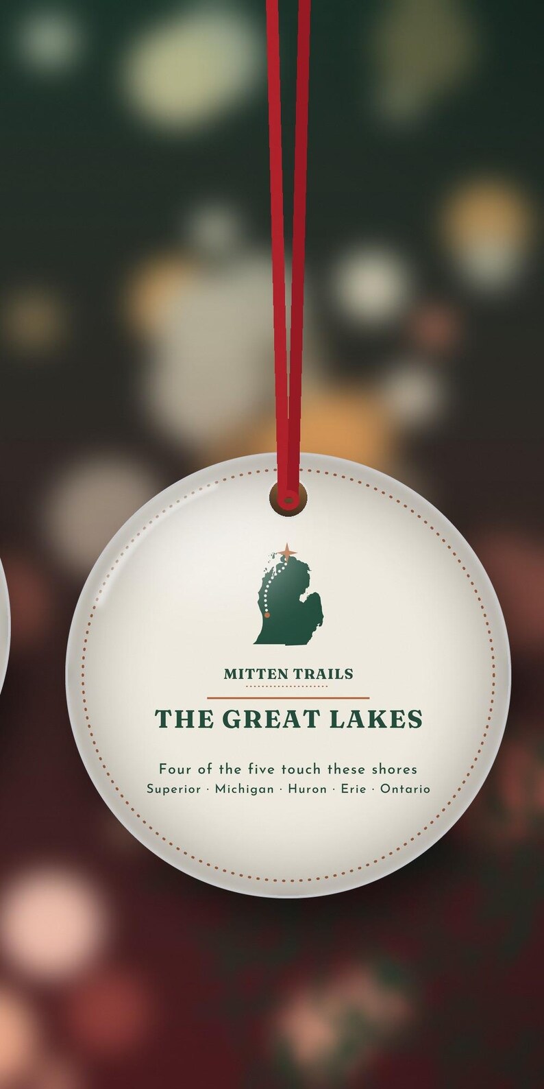 May include: A round white ornament hanging from a red ribbon. It features a green silhouette of Michigan with a red star and dotted line, the text MITTEN TRAILS, THE GREAT LAKES, and Four of the five touch these shores Superior Michigan Huron Erie Ontario.