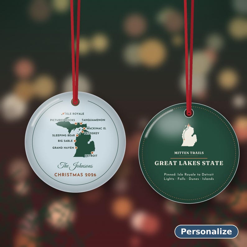 May include: Two round Christmas ornaments with red hanging strings. The left ornament is light blue with a map of Michigan, location markers, the text The Johnsons and CHRISTMAS 2026. The right ornament is dark green with a white Michigan map, MITTEN TRAILS, GREAT LAKES STATE and text.