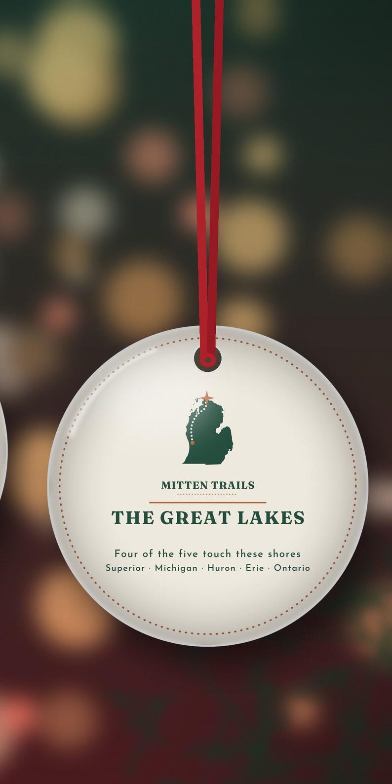 May include: A round, off-white hanging ornament with a red ribbon. It features a green silhouette of Michigan, the text "MITTEN TRAILS," "THE GREAT LAKES," and "Four of the five touch these shores Superior Michigan Huron Erie Ontario."