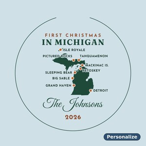 May include: A circular ornament featuring a dark green map of Michigan on a light blue background. Text reads FIRST CHRISTMAS IN MICHIGAN, The Johnsons, and 2026. Orange dots mark locations including Detroit, Grand Haven, and Isle Royale.