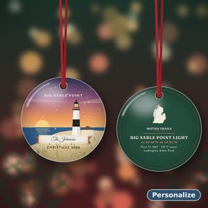 May include: Two round ornaments with red hanging strings. The left ornament shows a lighthouse at Big Sable Point, the text The Johnsons, and Christmas 2026. The right ornament is dark green with a map of Michigan, Mitten Trails, and Big Sable Point Light details.