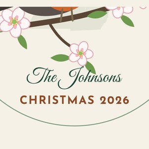 May include: A circular ornament featuring a brown bird perched on a branch with pink blossoms and green leaves. The text reads The Johnsons in dark green script and CHRISTMAS 2026 in brown block letters on a cream background.