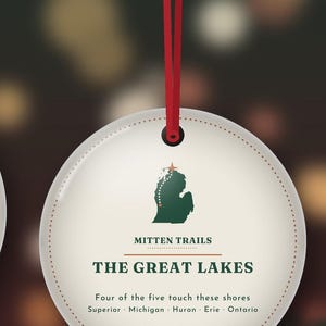 May include: A round, cream-colored hanging ornament with a red ribbon. It features a green map of Michigan, the text "MITTEN TRAILS," "THE GREAT LAKES," and "Four of the five touch these shores Superior Michigan Huron Erie Ontario."