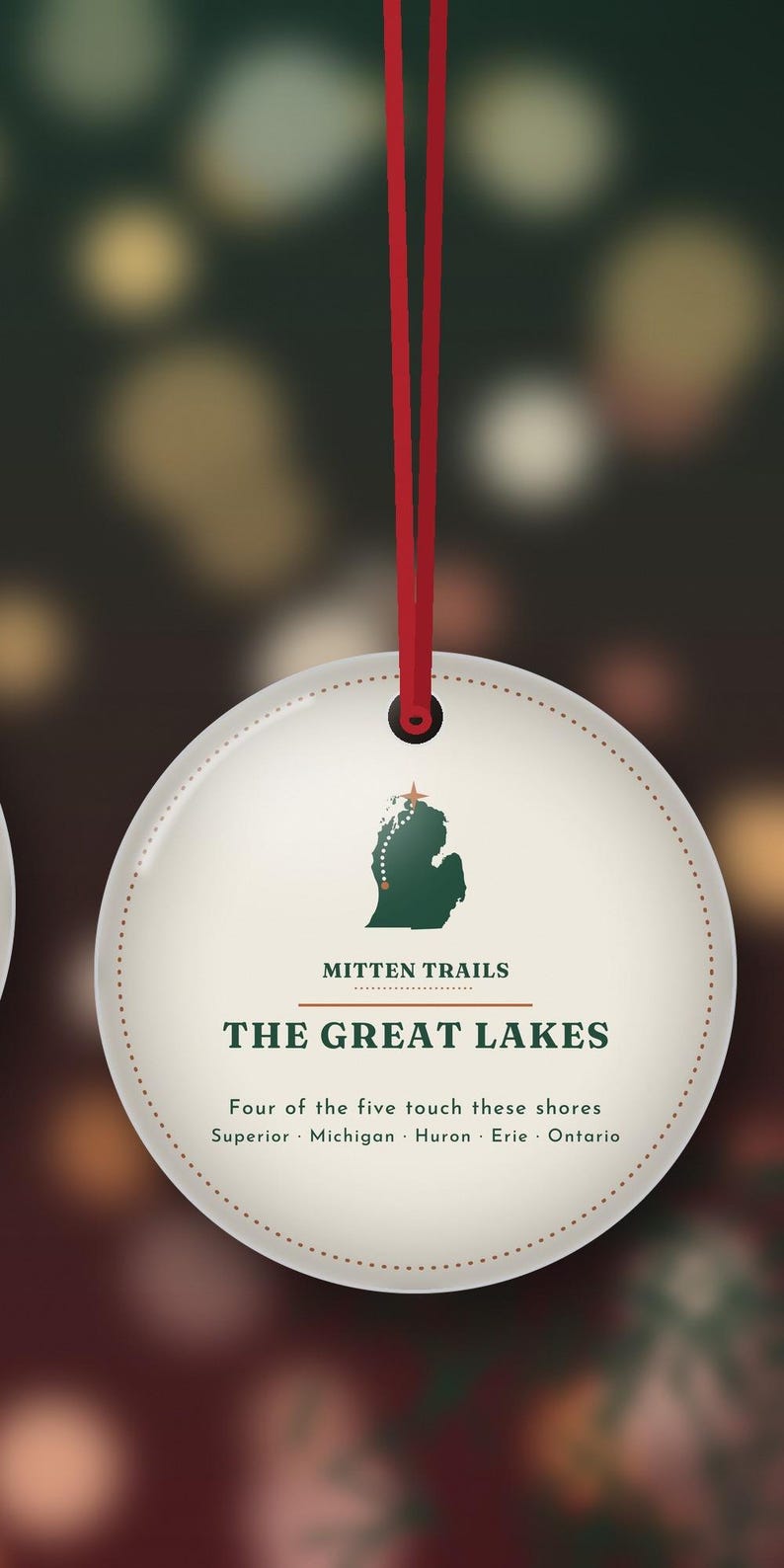 May include: A round, cream-colored hanging ornament with a red ribbon. It features a green map of Michigan, the text "MITTEN TRAILS," "THE GREAT LAKES," and "Four of the five touch these shores Superior Michigan Huron Erie Ontario."