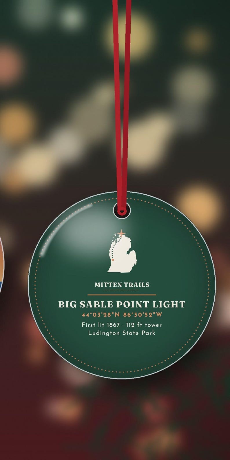 K&ouml;nnte beinhalten: Ein runder, dunkelgr&uuml;ner Anh&auml;nger an einem roten Band. Er zeigt eine wei&szlig;e Karte von Michigan mit einem Stern, den Text MITTEN TRAILS, BIG SABLE POINT LIGHT, 44&deg;03'28"N 86&deg;30'52"W, First lit 1867, 34 m tower und Ludington State Park.
