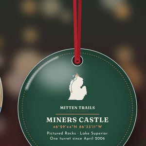 K&ouml;nnte beinhalten: Ein runder, dunkelgr&uuml;ner Anh&auml;nger an einem roten Band. In der Mitte befindet sich eine wei&szlig;e Karte von Michigan mit einem Stern, der Text MITTEN TRAILS, MINERS CASTLE, die Koordinaten 46&deg;29'44"N 86&deg;33'11"W, Pictured Rocks, Lake Superior und One turret since April 2006.