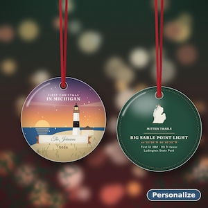 Puede incluir: Dos adornos redondos de cer&aacute;mica con cordones rojos. Uno muestra un faro, un atardecer y el texto First Christmas in Michigan, The Johnsons, 2026. El otro es verde oscuro con un mapa de Michigan, Mitten Trails y Big Sable Point Light.