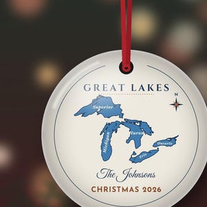 May include: A round white ceramic ornament hanging from a red ribbon. The design features a blue map of the Great Lakes labelled Superior, Michigan, Huron, Erie, and Ontario. Text reads GREAT LAKES, The Johnsons, and CHRISTMAS 2026.